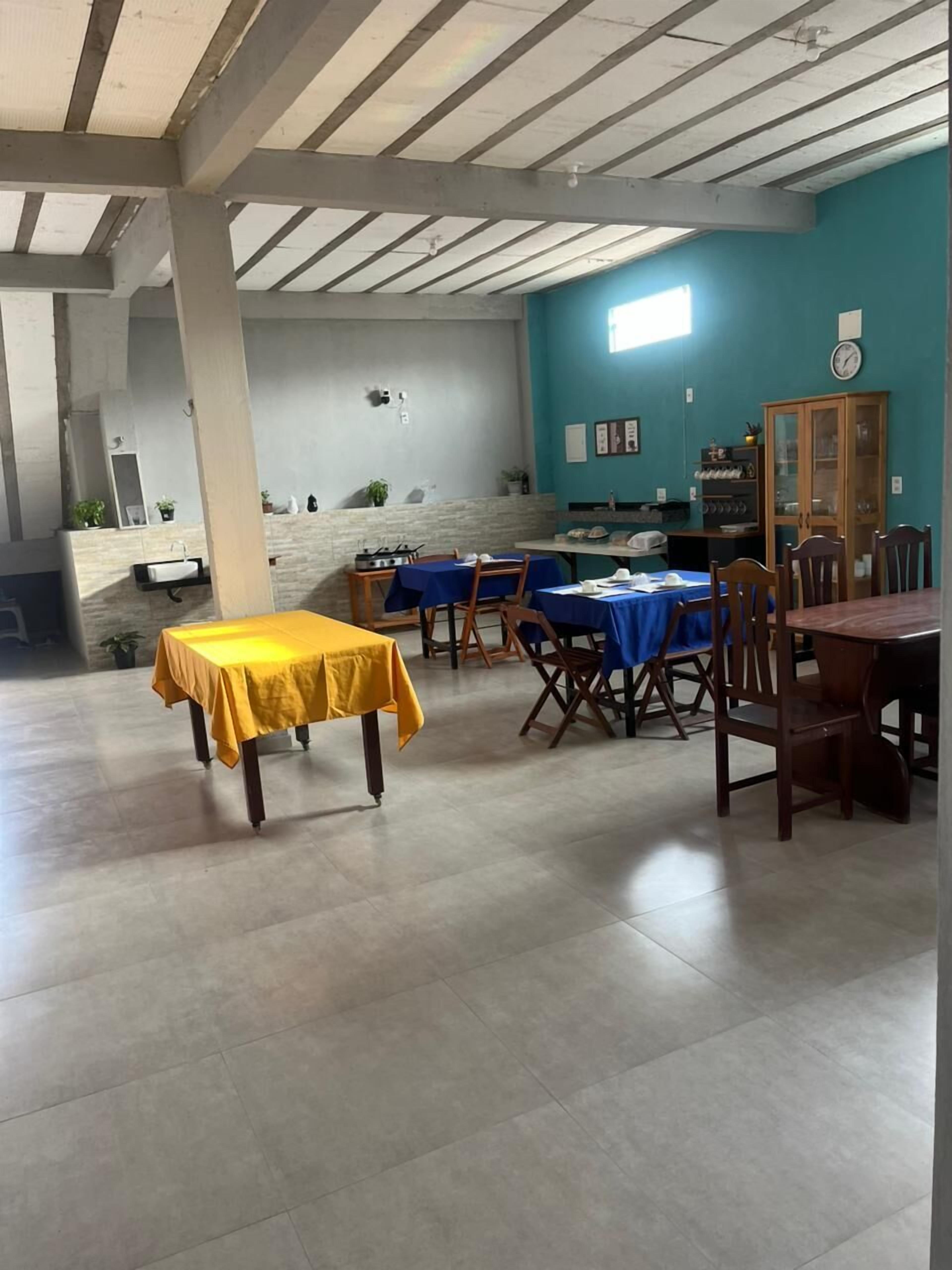 Una zona de menjador amb taules i caires, una cuina i un rellotge a la paret.