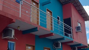 A two-story building with a red and blue facade, balconies with railings, and a small garden area with potted plants. - Pousada BG Lençóis (Barreirinhas)