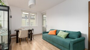 Een moderne woonkamer met een groene bank, een eettafel met stoelen en een glazen kast.