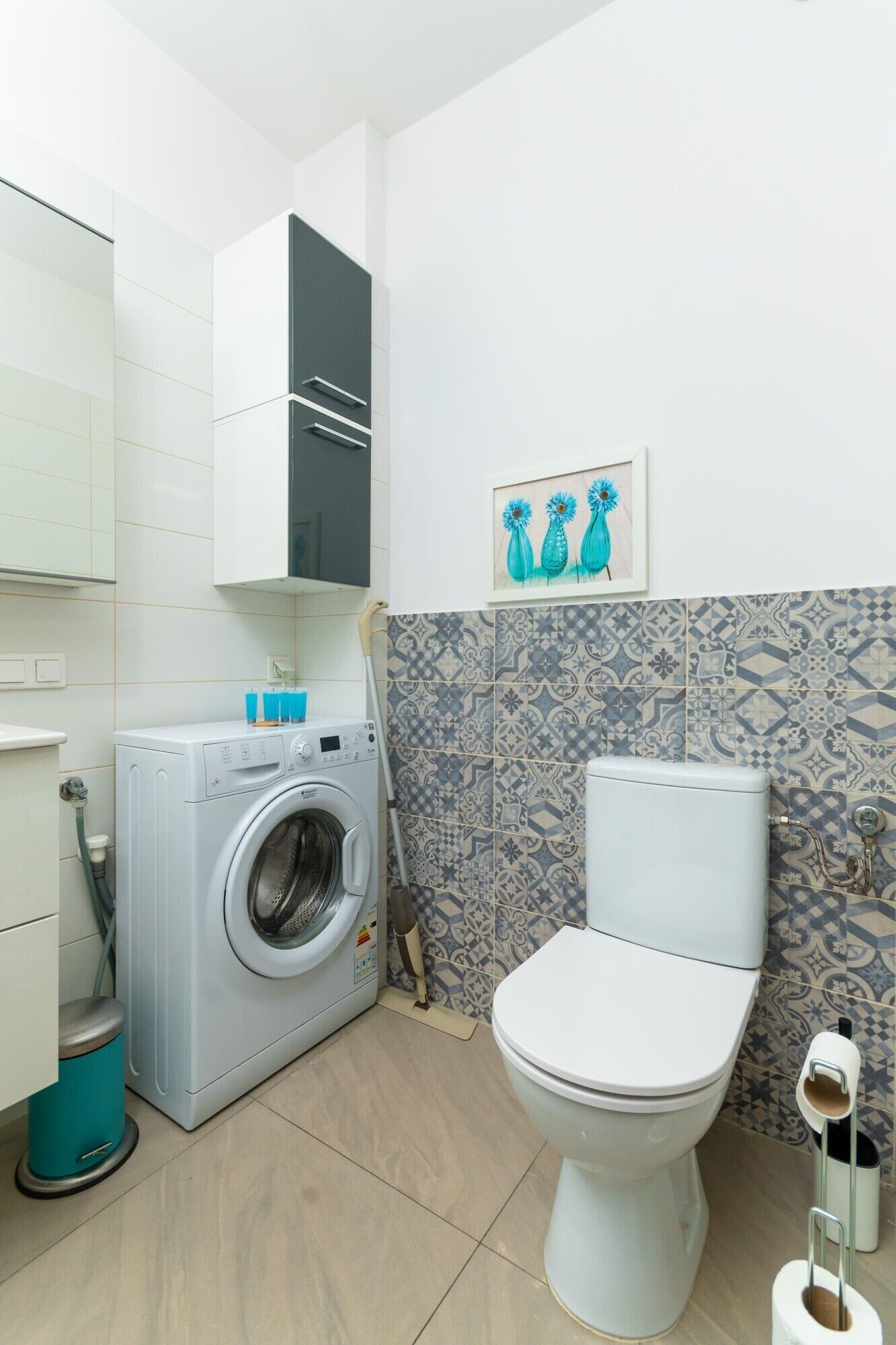 Een kleine badkamer met een wasmachine, toilet en tegels met een patroon.