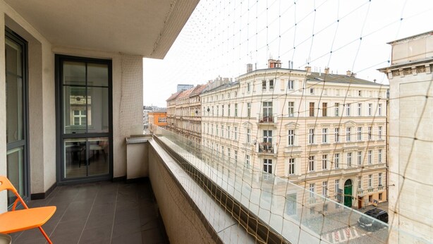 Een balkon met glazen hekwerk, met uitzicht op een historisch gebouw.