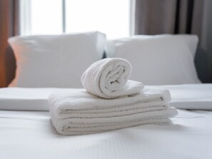 A neatly made bed with white linens and a rolled towel on top.