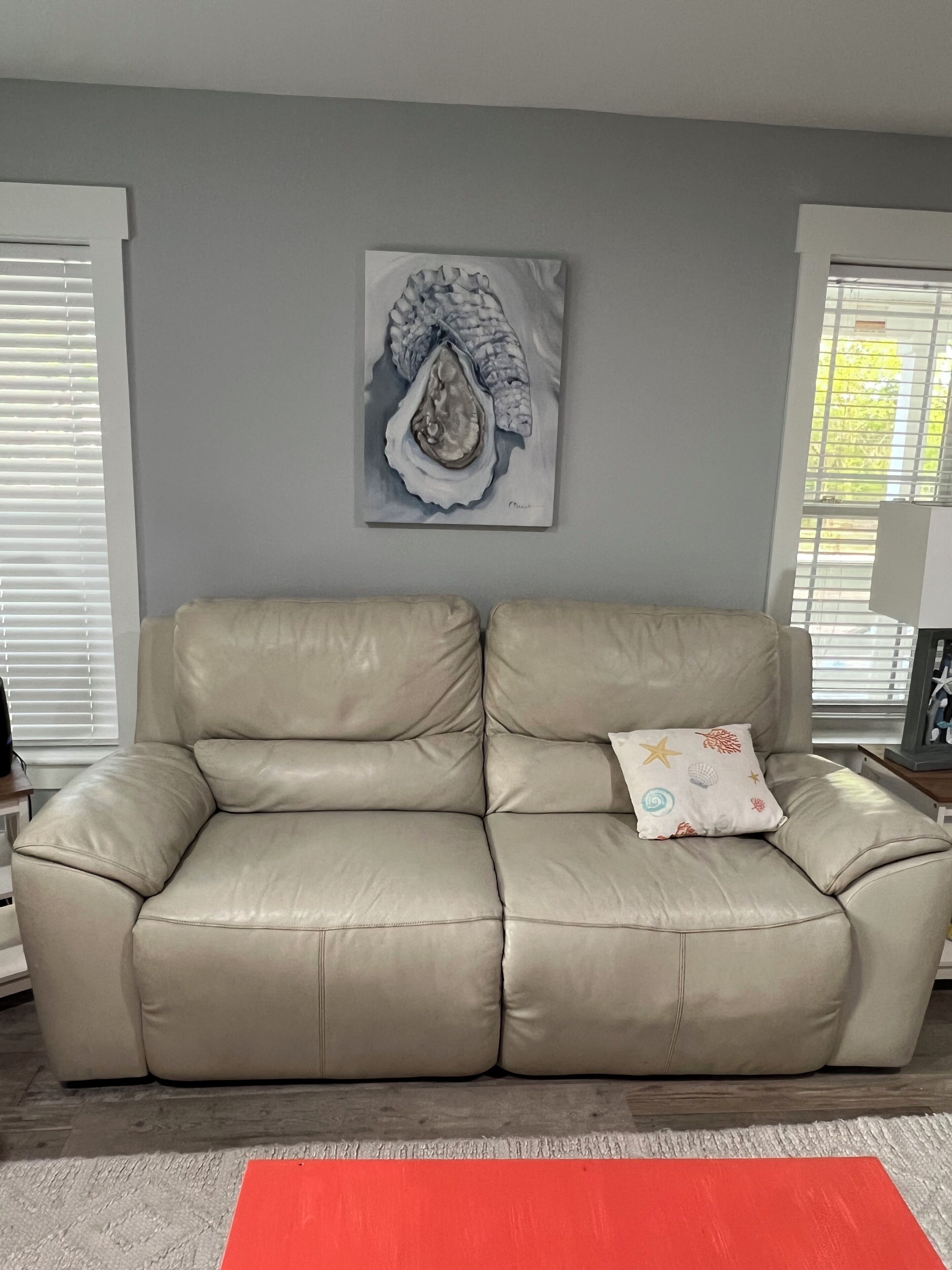 A beige leather sofa with a decorative pillow, a gray wall with a framed artwork, and a red rug on a wooden floor.