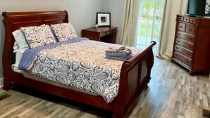 A wooden bed with a patterned bedspread, a nightstand with a framed picture, and a wooden dresser with drawers.