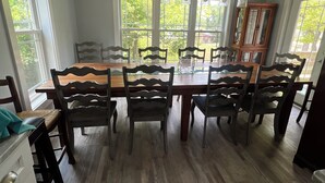 A dining area with a wooden table and chairs, large windows, and a ceiling light fixture.