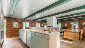 Una cocina con pared de ladrillo, una isla grande con pileta y un área de comedor con mobiliario de madera.