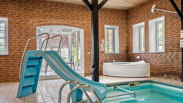 Una piscina interior con tobogán, jacuzzi y pared de ladrillo.