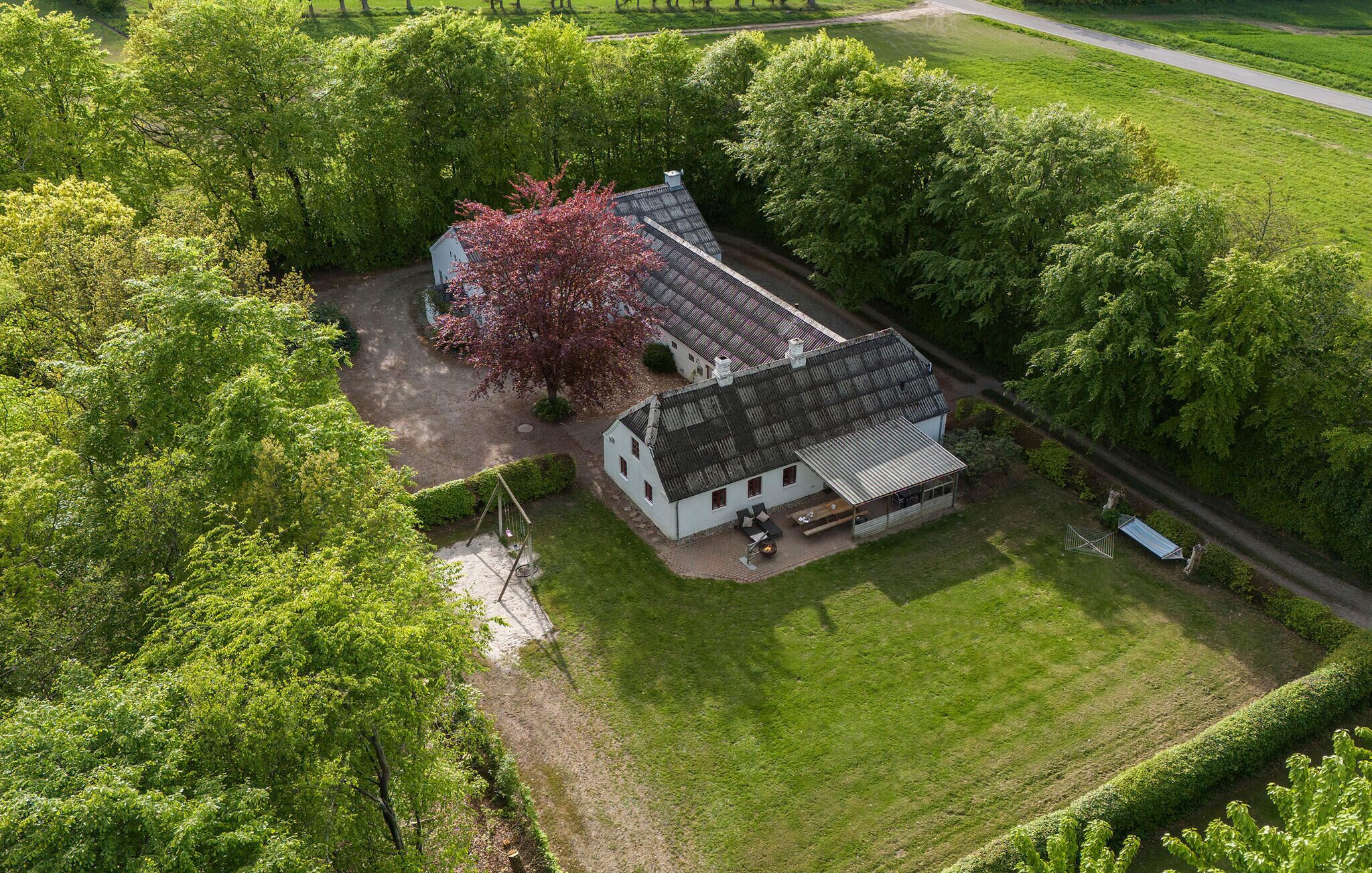 Une maison blanche avec un toit en pente, entourée d’une végétation luxuriante et d’une pelouse bien entretenue.