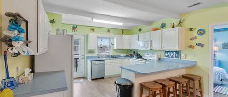 A modern kitchen with white cabinets, a central island with stools, and a trash can.