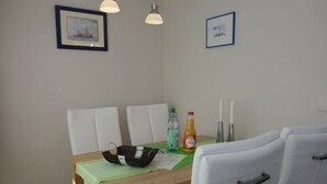 A dining area with a wooden table, white chairs, a green tablecloth, a black basket, a bottle of orange juice, and two candles. - Haus Teunis - Vacation in the best location, in the pedestrian zone in Wyk - Teunis (Wyk auf Föhr)