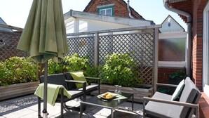 A patio with outdoor furniture, a table with a basket of fruit, and a green umbrella. - Haus Teunis - Vacation in the best location, in the pedestrian zone in Wyk - Teunis (Wyk auf Föhr)