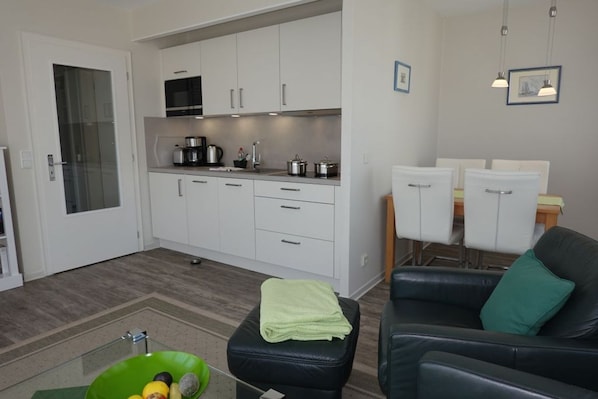 A compact living space with a kitchenette, a dining area, and a seating area with a sofa and ottoman.