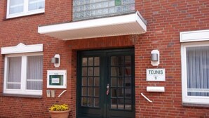 Ein Backsteinhaus mit einer dunkelgrünen Tür, einem Schild mit der Aufschrift „TEUNIS 9“ und einem Fenster mit Gittermuster.