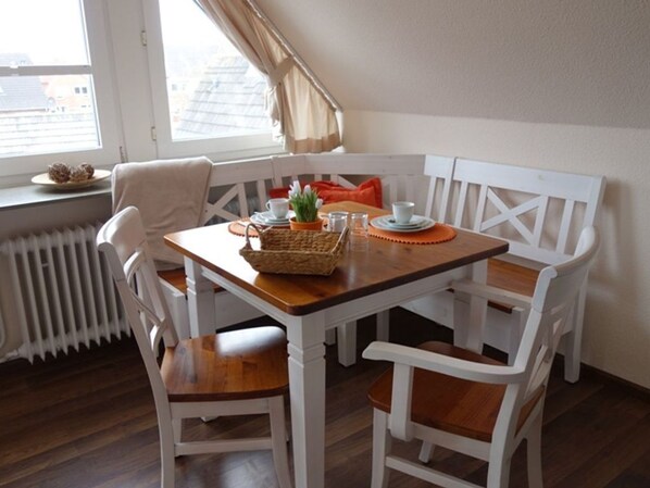 A dining area with a wooden table and white chairs, a radiator, and a window with curtains.