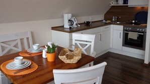 Eine kleine Küche mit weißen Schränken, einem Holzespeisesaal mit Tellern, Besteck und einem Korb.