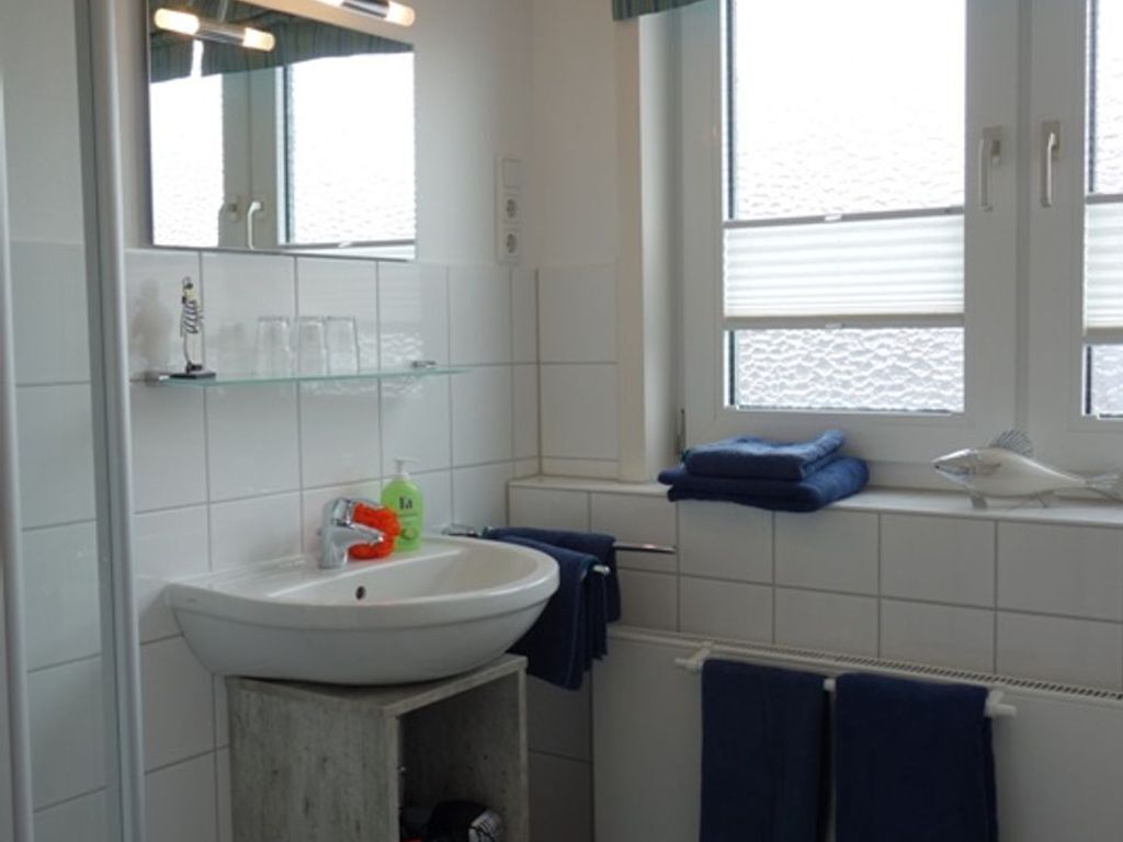 Een badkamer met een witte wastafel, een spiegel en een raam met uitzicht op zee.