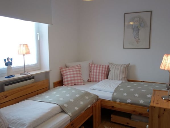 A bedroom with two single beds, a desk with a lamp, and a window with a view.