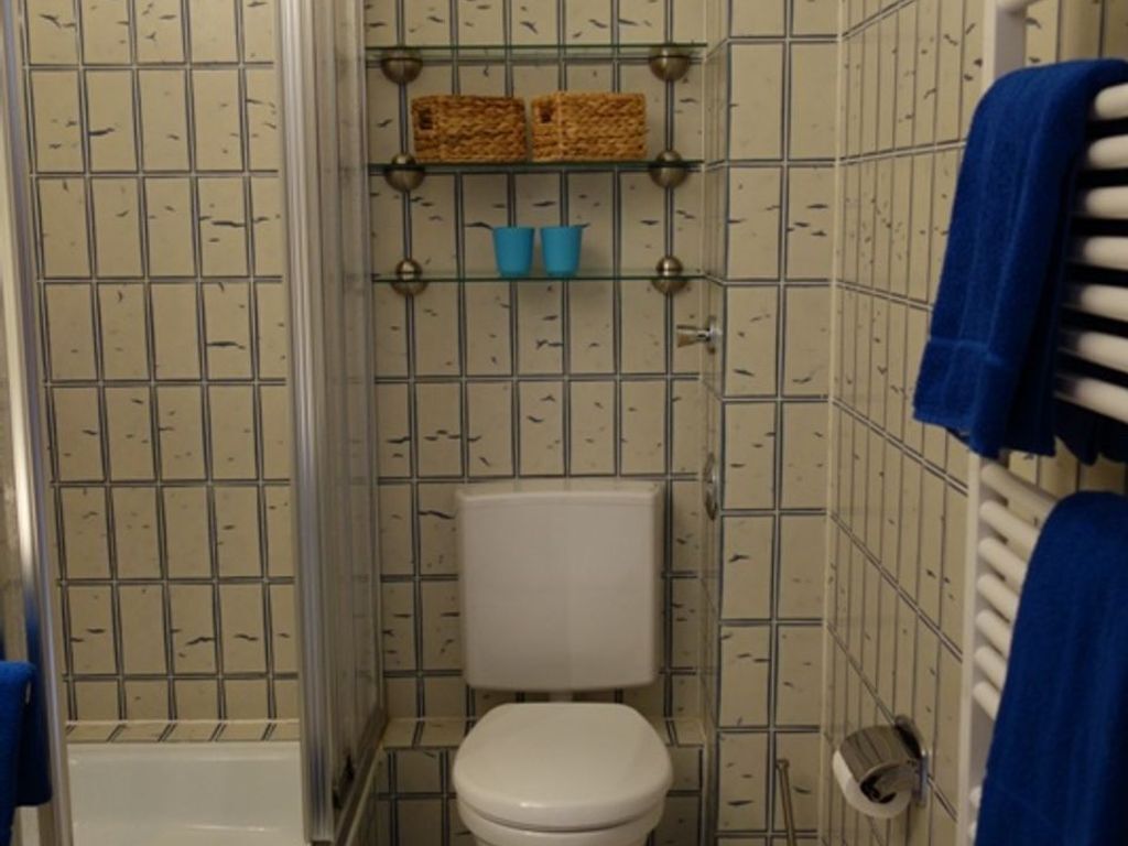 Ein kleines Badezimmer mit Toilette, Dusche und Ablageflächen mit Körben und Bechern.