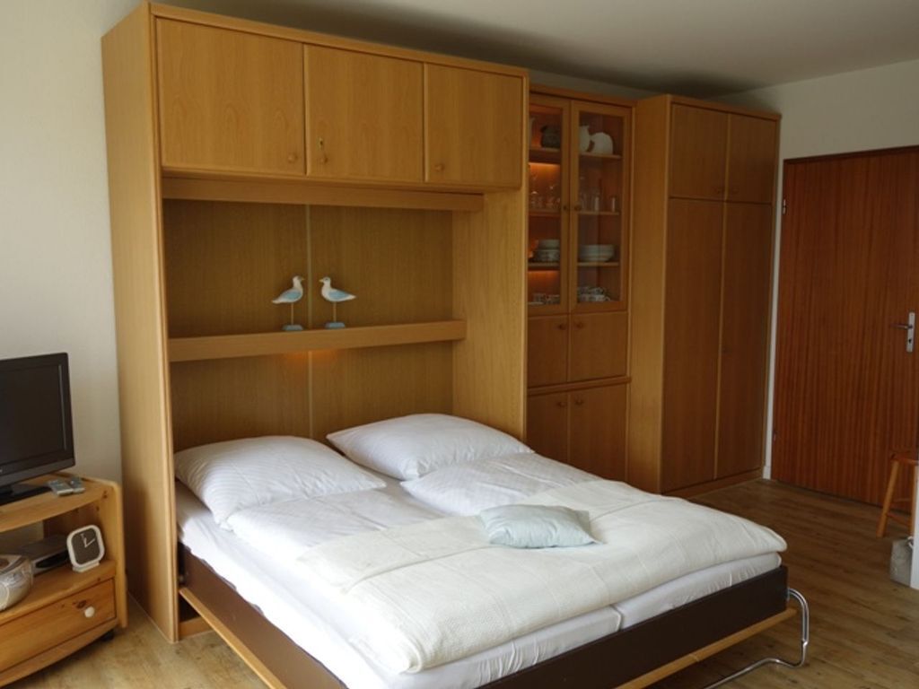 Une chambre à coucher avec un lit, une armoire en bois et un téléviseur posé sur une table de chevet en bois.