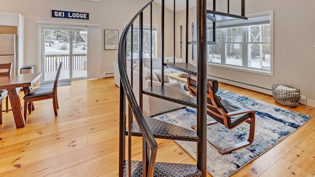 Ein modernes Interieur mit Holzboden, einem Essbereich, einer Treppe mit Metallgeländer und einem Schild mit der Aufschrift 'SKI LODGE'.