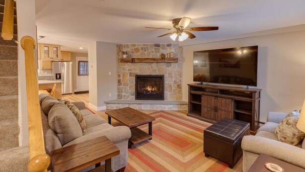 A living room with a stone fireplace, a flat-screen TV, a wooden coffee table, and a sofa. - Loon Condo with Fireplace (Woodstock)