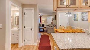 A kitchen with granite countertops, wooden cabinets, and a red rug leading to a dining area with yellow chairs. - Loon Condo with Fireplace (Woodstock)