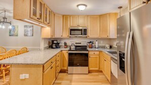 A kitchen with wooden cabinets, a stainless steel refrigerator, a microwave, and a stove. - Loon Condo with Fireplace (Woodstock)