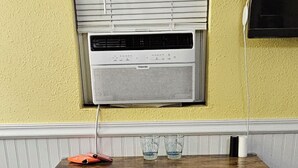 A compact kitchen with a white countertop, two black stools, and an air conditioning unit above. - River Bunkie (Tivoli)