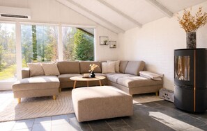 Una sala de estar moderna con un sofá modular, una mesita redonda, un mueble de entretenimiento negro y vistas a árboles a través de amplios ventanales.