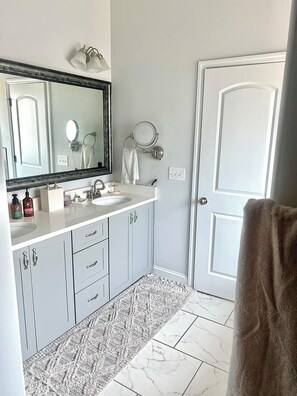 A bathroom with a white sink, mirror, and towel rack. There is a patterned rug on the floor and a white door.