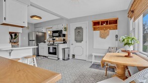 Une cuisine moderne avec des meubles blancs, un four encastré et un coin repas comprenant une table en bois et des chaises blanches.