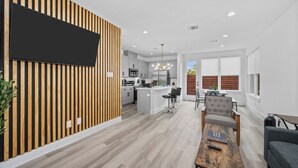 A modern kitchen with a central island, a dining area with a wooden table, and a living room with a sofa.