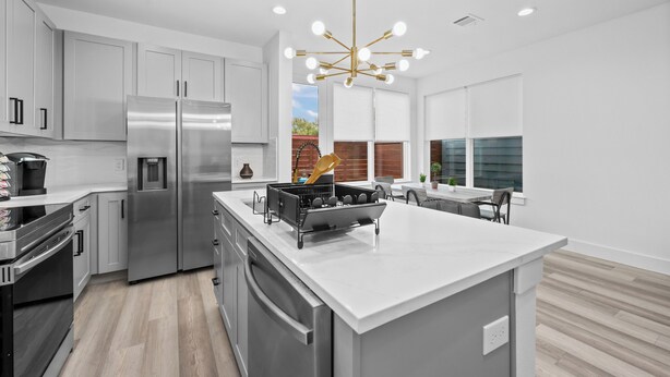 A modern kitchen with stainless steel appliances, a central island, and a contemporary chandelier.