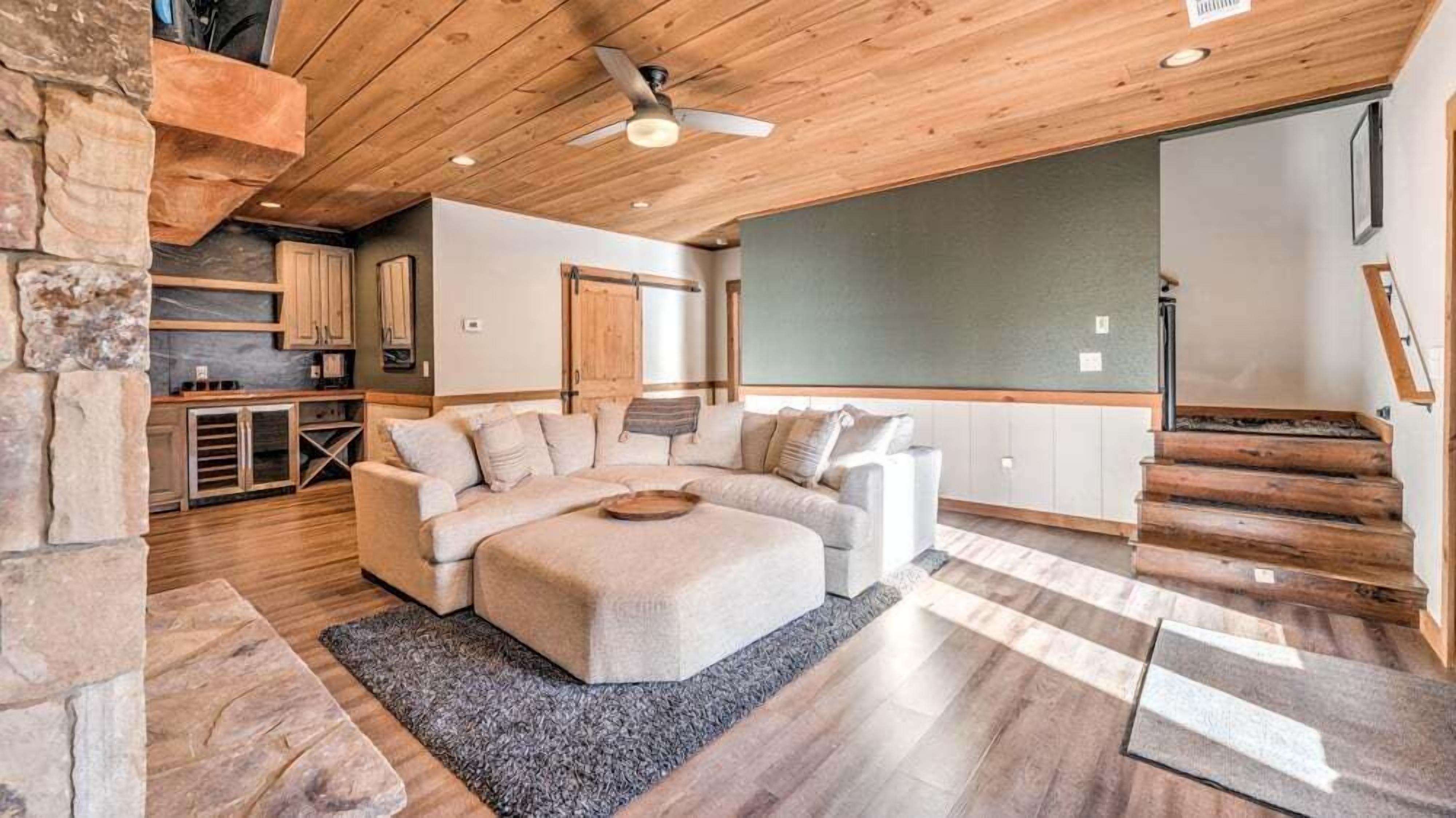 A spacious living area with a large L-shaped sectional sofa, a wooden ceiling, and a stone accent wall.