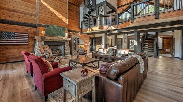A spacious living room with a fireplace, a high ceiling, and a balcony.