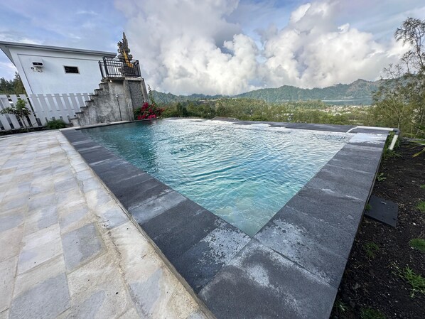 A swimming pool with a stone border and a view of a mountain range in the background. - Batur Exotic (Kintamani)