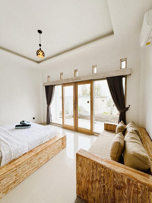 A modern bedroom with a large window, a wooden bed frame, a sofa, and a ceiling light. - Batur Exotic (Kintamani)