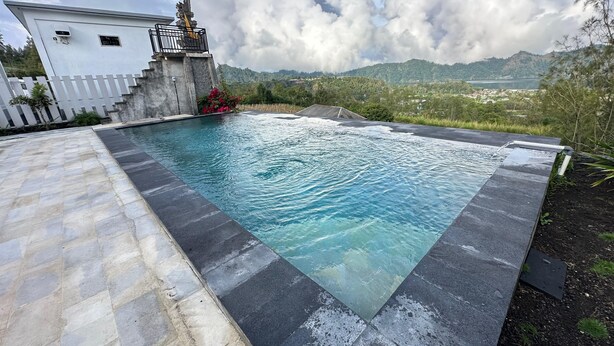 Une piscine bordée de pierres, une statue et une vue sur les montagnes et une ville lointaine.