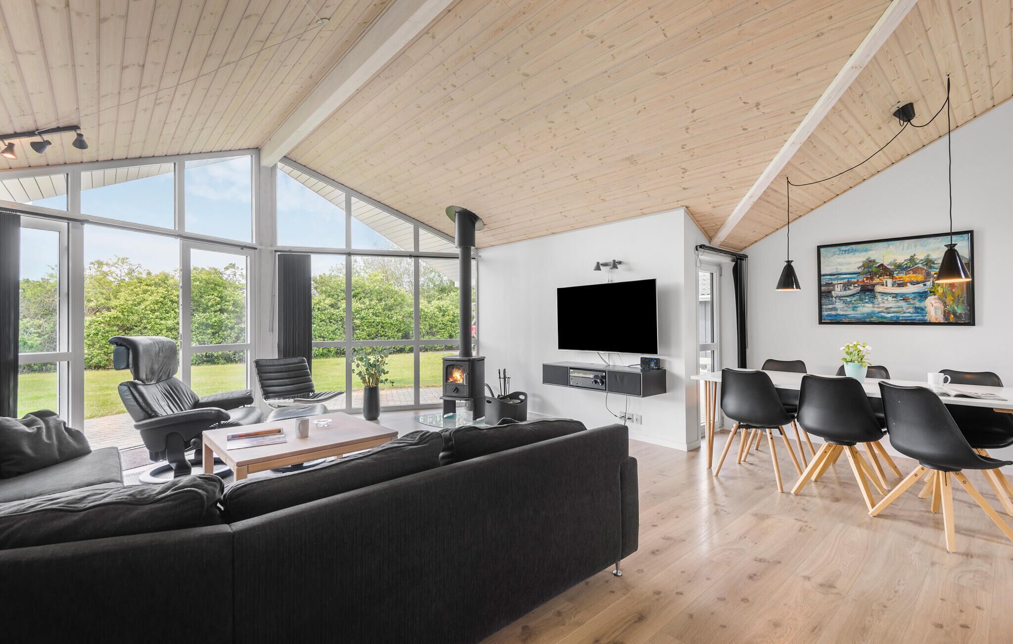 Uma sala de estar moderna com um sofá grande, uma área de jantar com mesa e cadeiras, uma lareira e uma TV fixada na parede.