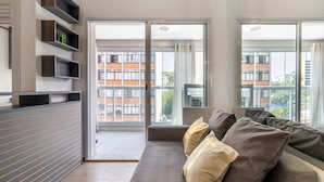 Un soggiorno moderno con un divano, una libreria a parete e ampie porte scorrevoli in vetro che si aprono su un balcone.