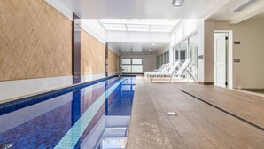 Una piscina con pareti piastrellate e pavimento in legno, che conduce a una zona relax con sedie e una porta.