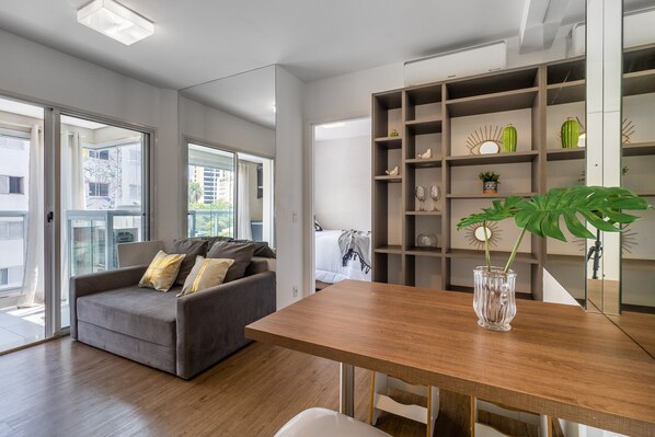 Een moderne woonkamer met een grijze bank, houten vloer en een eettafel met een vaas.