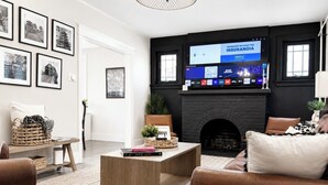 Olohuone, jossa on takka, sen yläpuolella seinälle asennettu televisio ja seinällä kehyksiin asetettuja valokuvia.