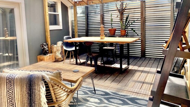 Een overdekt terras met een houten tafel en stoelen, potplanten en een decoratieve Boeddhabeeld.