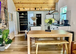 A modern kitchen with wooden cabinetry, a blackboard sign, and a dining area with a wooden table and bench. - Sweet Bungalow. Super Location. Walkability (Austin)