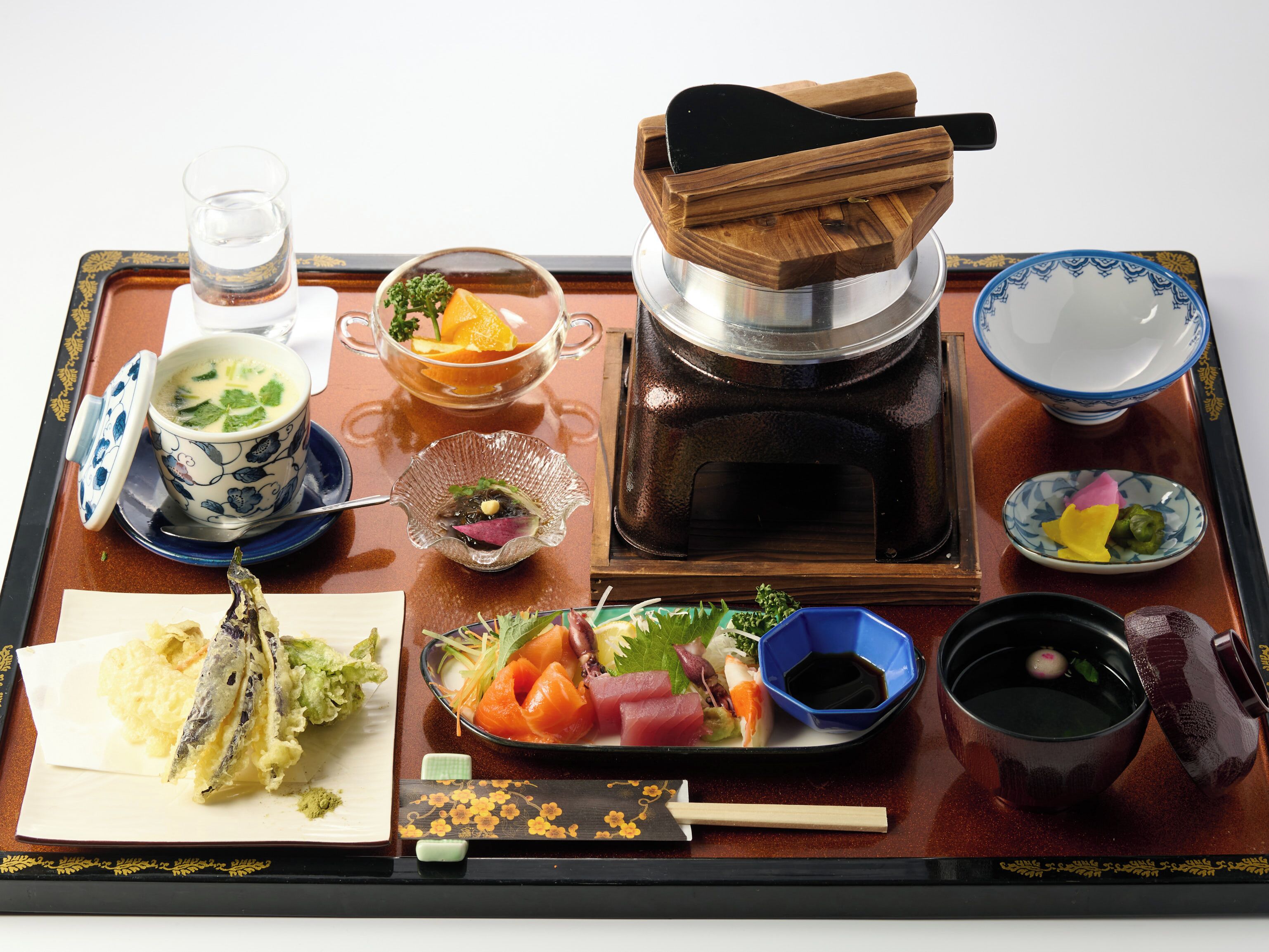 A tray with various Japanese dishes including sushi, soup, and a hot pot.