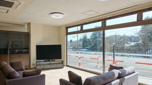 A living room with a large window, a flat-screen TV, and two sofas. - Owara View Hotel (Toyama)
