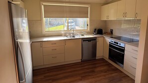 Ett modernt kök med ett kylskåp i rostfritt stål, en diskmaskin, en ugn och ett fönster med utsikt över omgivningen.