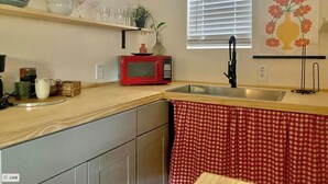 Een keuken met een rode magnetron, een gootsteen en een raam met jaloezieën.