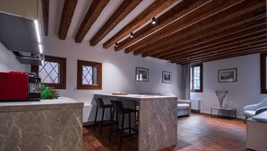 A modern kitchen with a marble island, wooden beams, and a red appliance.
